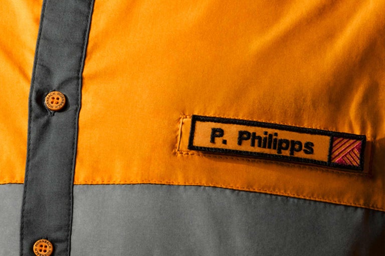 Detailný záber pracovného odevu s menovkou a logom Hornbach na gombíkoch