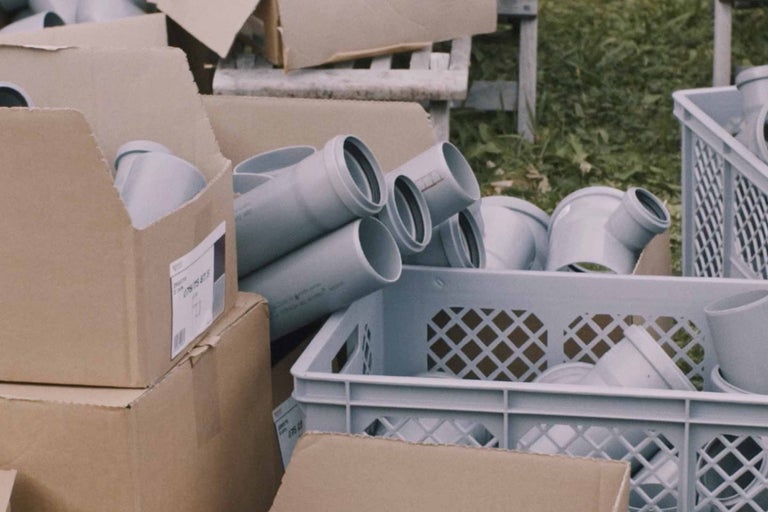 Sivé odpadové rúry a tvarovky v kartónoch a plastovej nádobe.