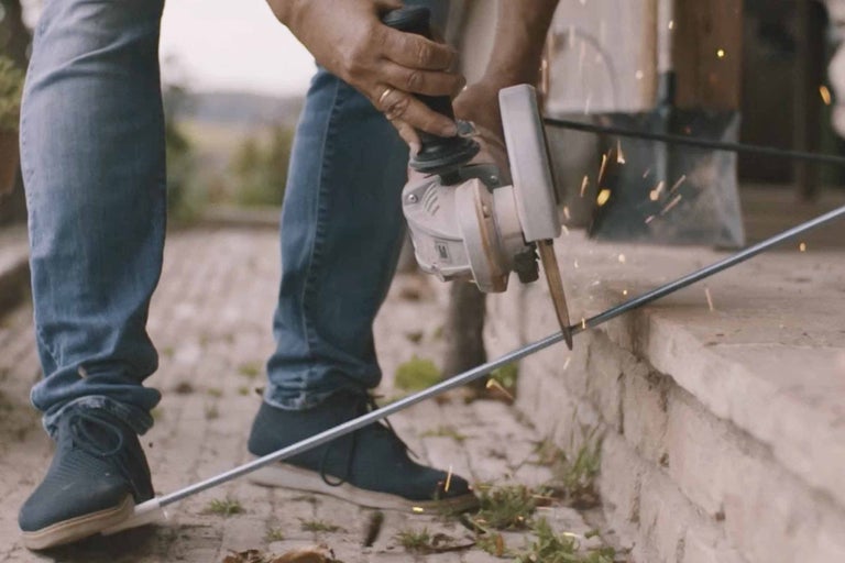 Osoba reže tyč uhlovou brúskou.