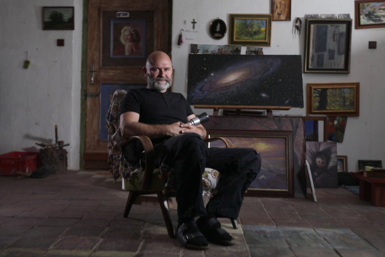 Muž sedí v kresle a je obklopený obrazmi.