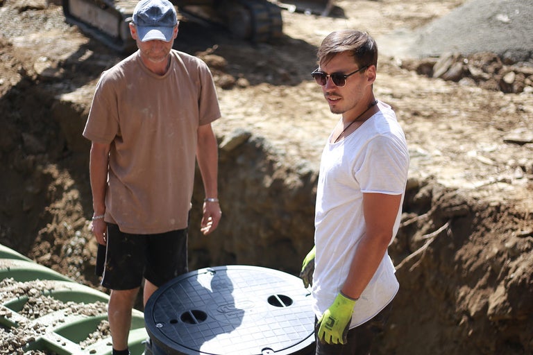 Dvaja stavební robotníci inštalujú žumpu na stavenisku.