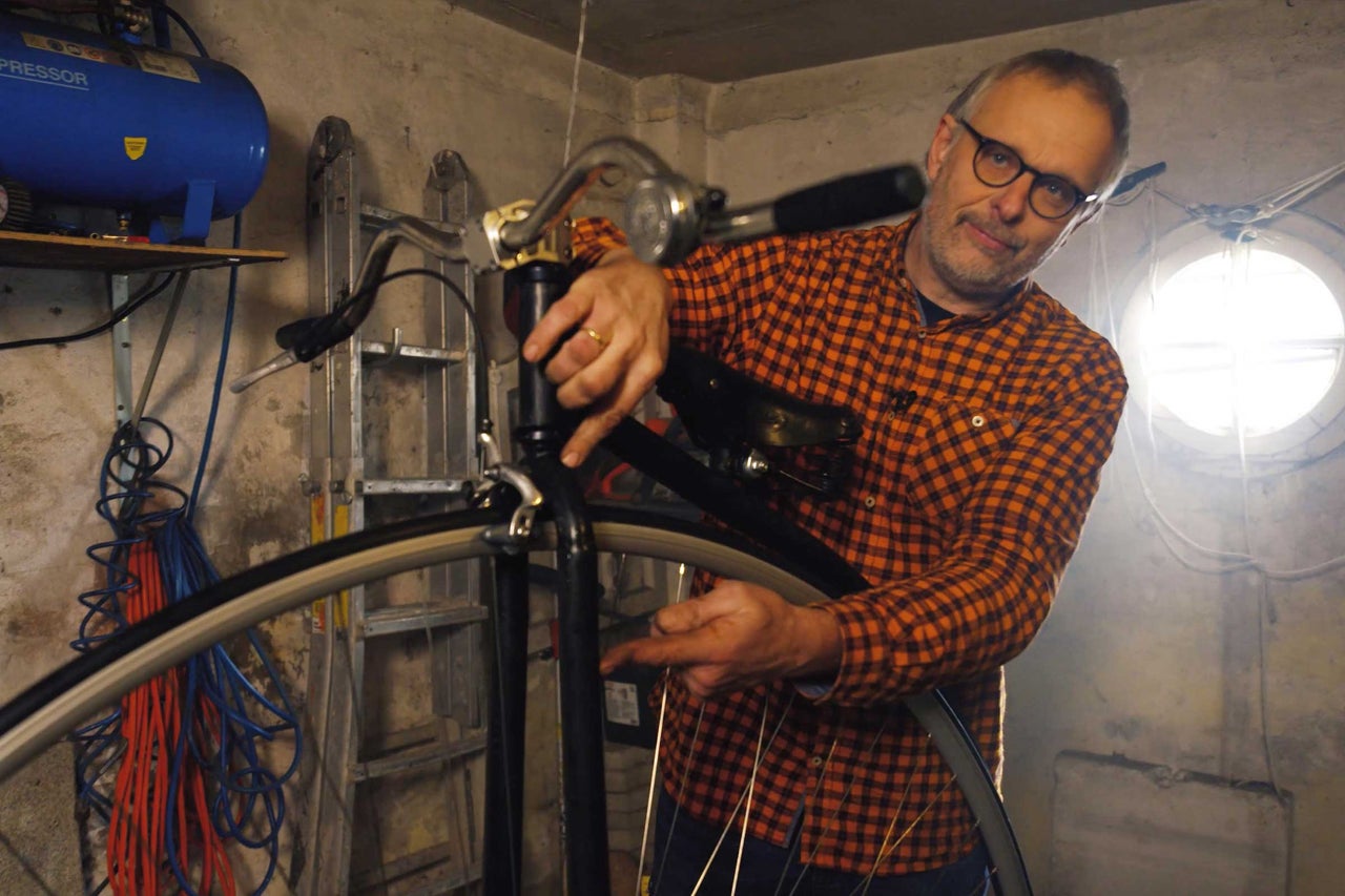 Muž opravuje bicykel v dielni s náradím a kompresorom