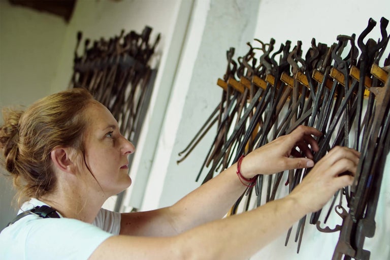 Žena upravuje radu kováčskych klieští na stene.