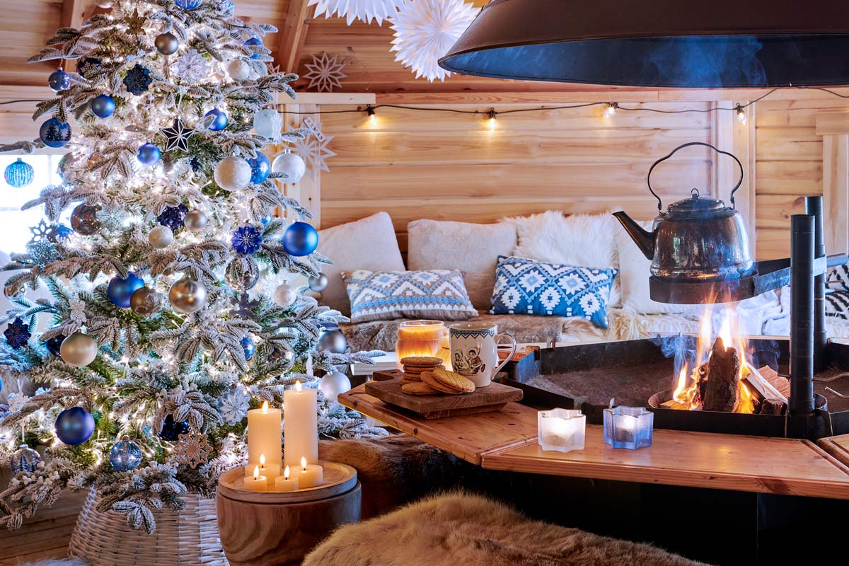 Útulná vianočná scéna so zdobeným stromčekom, ohňom v krbe a rustikálnym dreveným domom