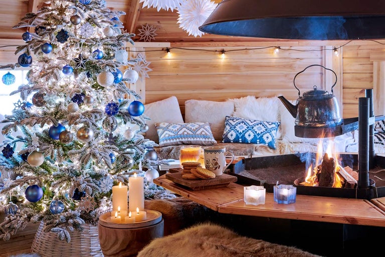 Útulná vianočná scéna so zdobeným stromčekom, ohňom v krbe a rustikálnym dreveným domom