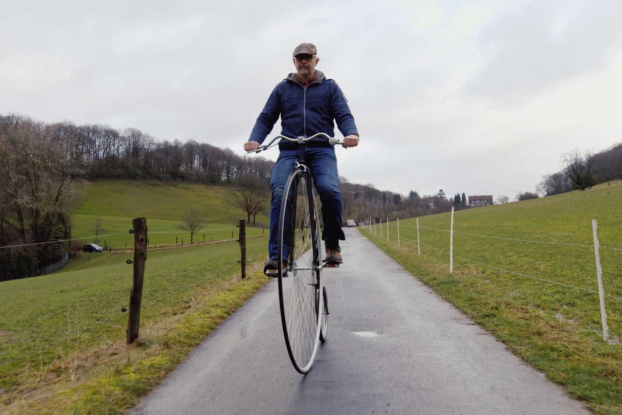 Muž jazdí na vysokom bicykli po vidieckej ceste