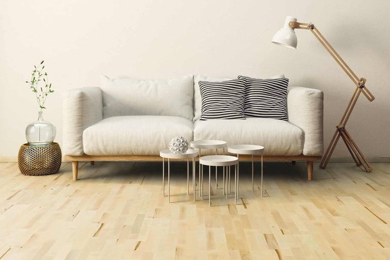 Obývacia izba s pohovkou, vankúšmi, príručnými stolíkmi, stojacou lampou a dekoráciou na drevenej podlahe.