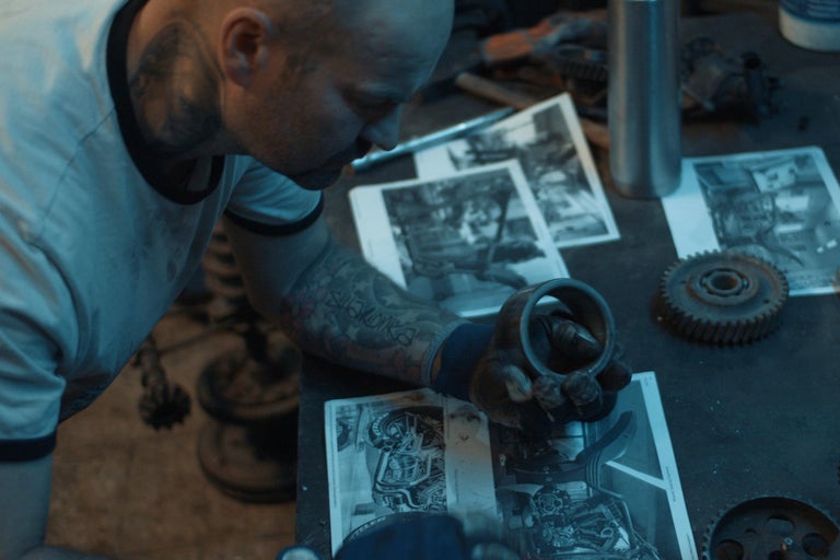 Muž v dielni si prezerá motocyklové diely a výkresy.