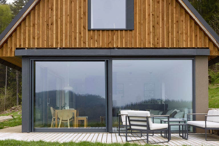 Moderný dom s drevenou fasádou, veľkými oknami a terasovým nábytkom