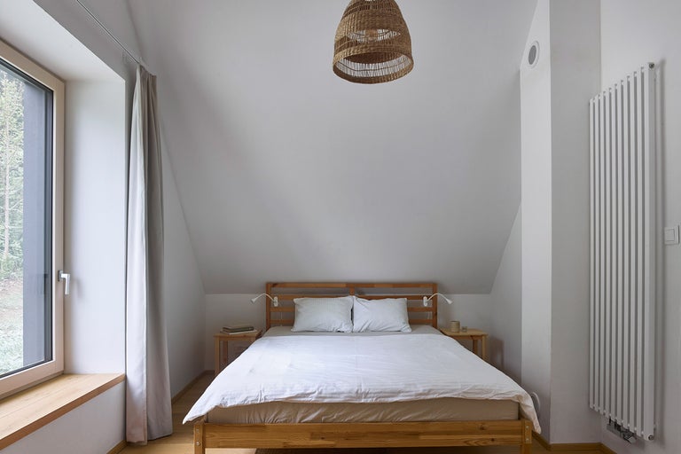 Spálňa s dreveným rámom postele, nočnými stolíkmi, radiátorom, oknom a slamenou lampou