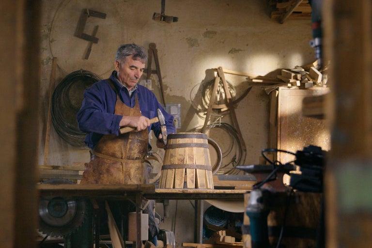 Remeselník vyrába v dielni drevený sud s kladivom.