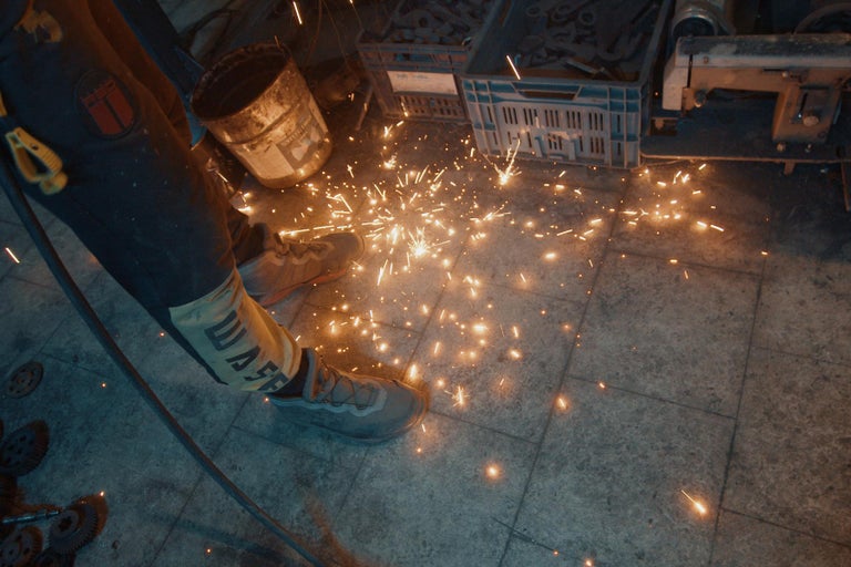 Iskry pri obrábaní kovu s pracovným odevom a bezpečnostnou obuvou.