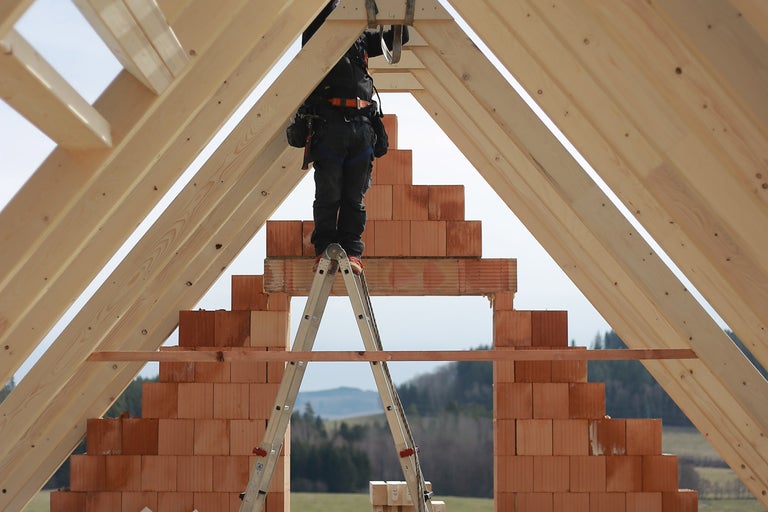 Stavebný robotník na rebríku pri stavbe domu z dreva a tehál.