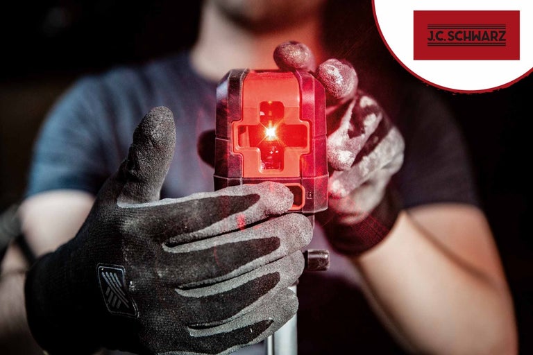 Pracovník v rukaviciach drží krížový čiarový laser. Logo J.C. Schwarz.