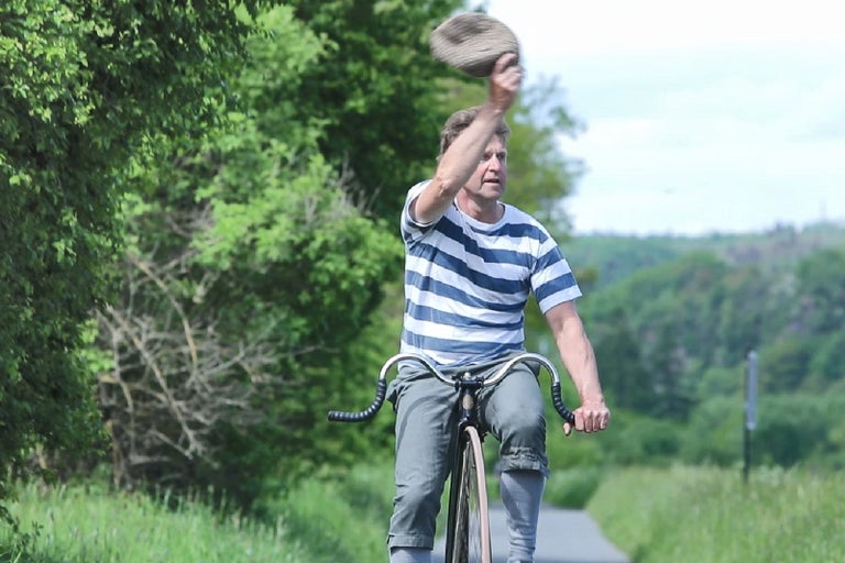 Muž na vysokom bicykli dvíha klobúk