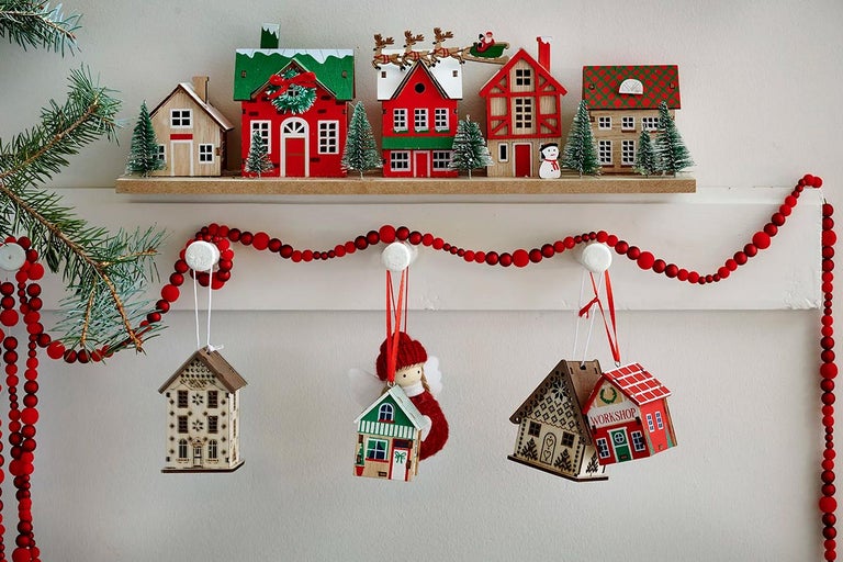 Ozdobné drevené domové ozdoby s červenou korálkovou girlandou na poličke