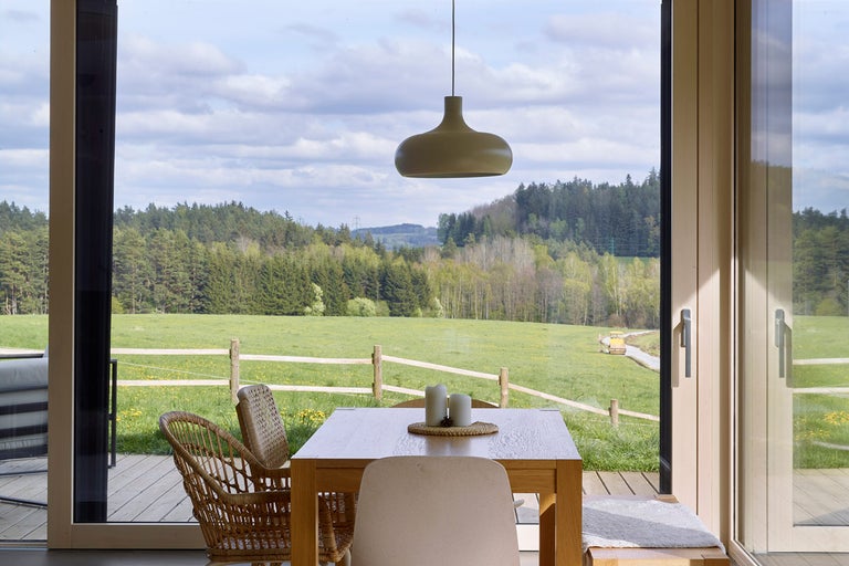 Svetlá jedáleň s dreveným stolom, stoličkami a výhľadom na zelenú krajinu