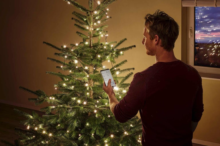 Muž ovláda svetelnú reťaz na vianočnom stromčeku pomocou smartfónu.