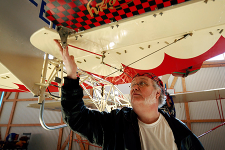 Muž kontroluje lietadlo v hangári. Lietadlo má červeno-biely dizajn.