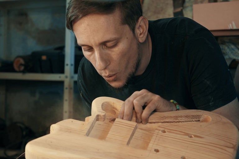 Muž pracuje v dielni na drevenom tele gitary.
