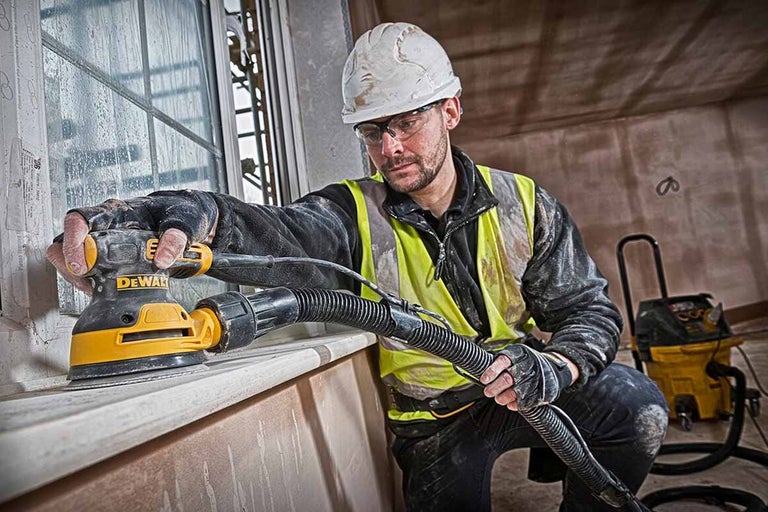 Remeselník brúsi okno excentrickou brúskou DeWalt, pripojené odsávanie prachu