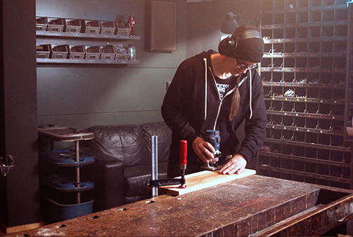 Muž frézuje drevenú dosku hornou frézou v dielni