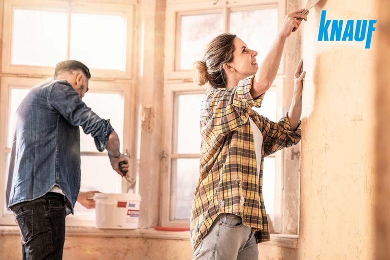 Žena a muž nanášajú sadru na stenu, logo Knauf.