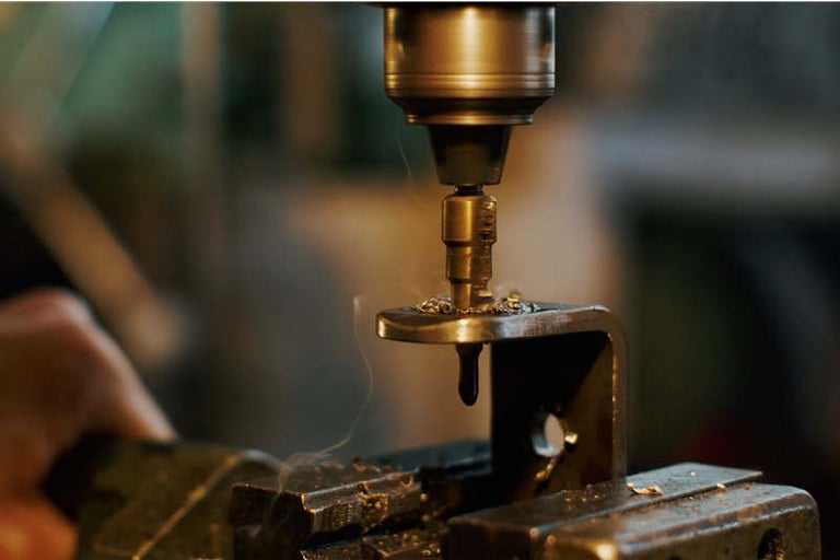 Detailný záber vŕtačky vŕtajúcej cez kov vo zveráku.