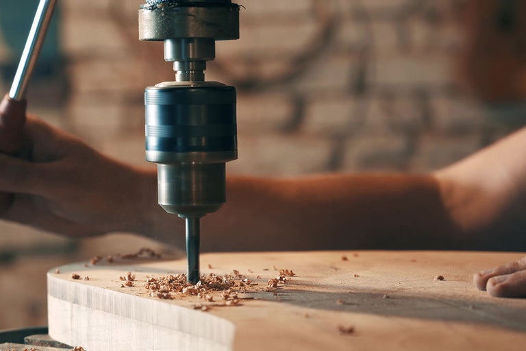 Detail stolnej vŕtačky vŕtajúcej do kusu dreva.