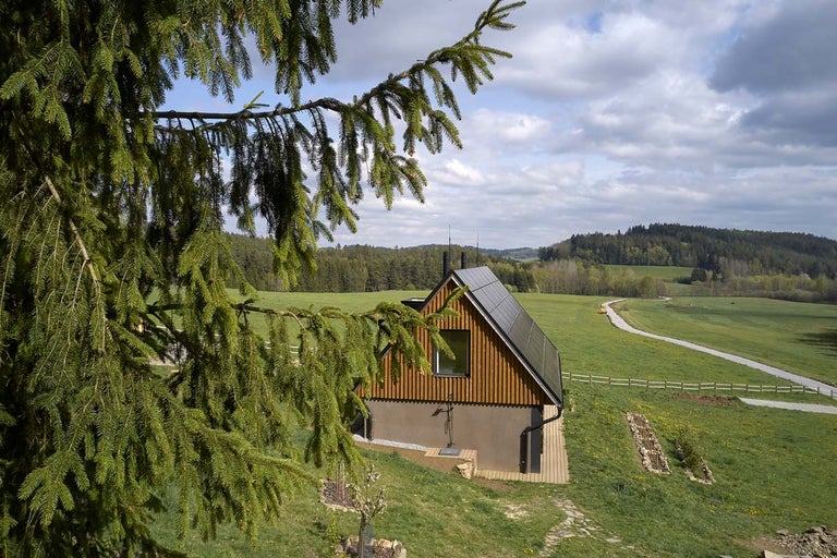 Moderný dom s drevenou fasádou a solárnym systémom vo vidieckom prostredí.