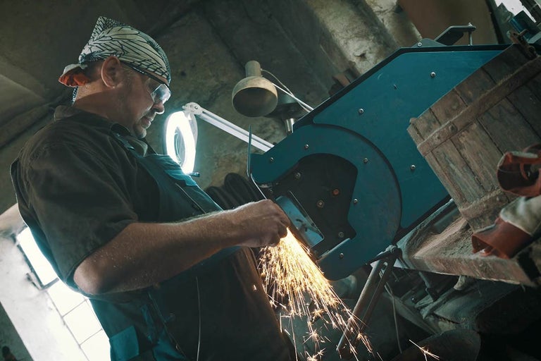 Muž brúsi kovový kus s brúskou, z ktorej lietajú iskry