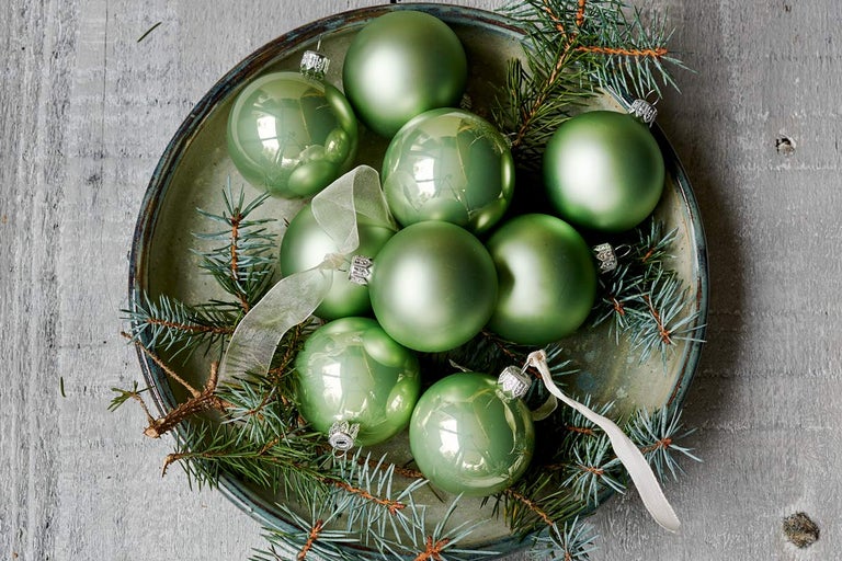 Zelené vianočné gule v miske s vetvami jedle a stuhami