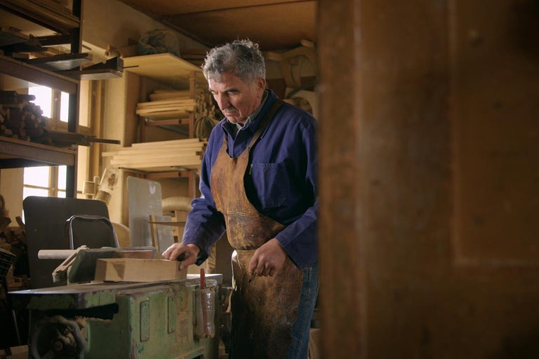 Remeselník pracuje s hobľovacím strojom v dielni plnej dreva.