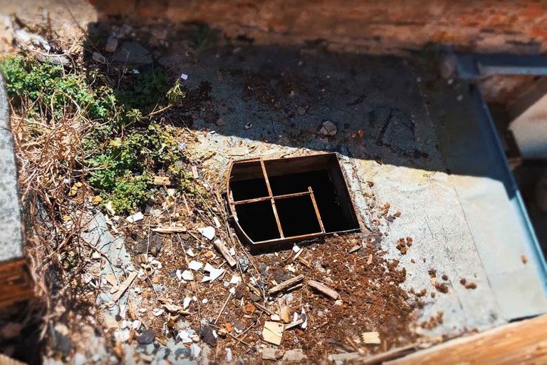 Kryt šachty s mrežou na pozemku s nečistotami a rastlinami.