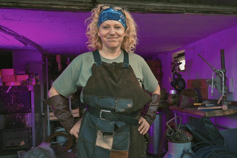 Žena nosí zásteru, kožené rukavice a čelenku v dielni