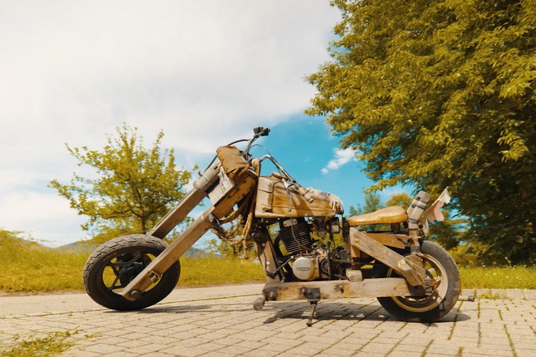 Drevená motorka na dláždenej ceste pred stromami a modrou oblohou