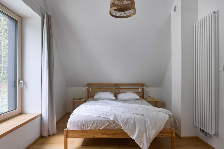 Spálňa s drevenou posteľou, nočnými stolíkmi a radiátorom pod stropnou lampou
