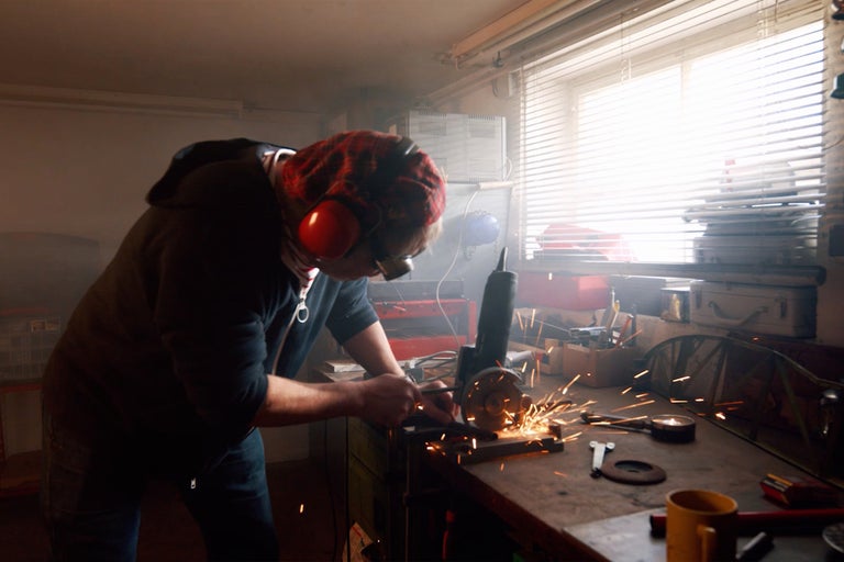 Muž pracuje s uhlovou brúskou v dielni, odletujú iskry.