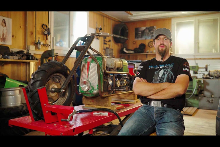 Dielňa s mužom pred neobvyklým motocyklom na červenom stole