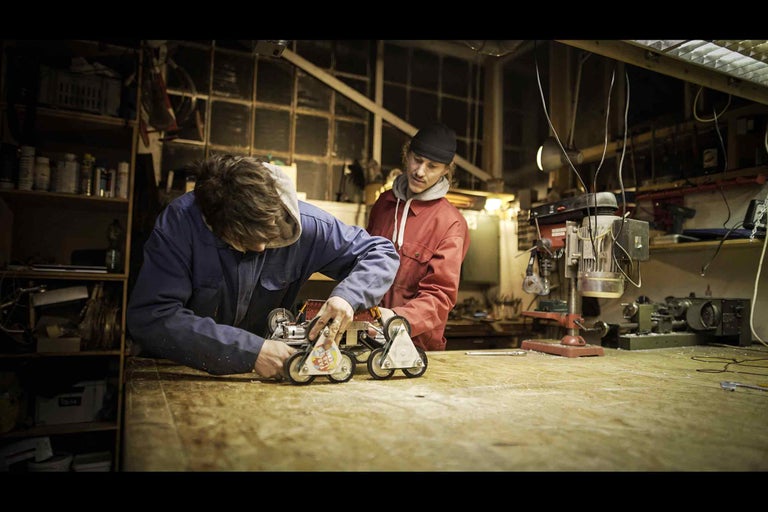 Dielňa s dvoma ľuďmi pracujúcimi na robotickom vozidle