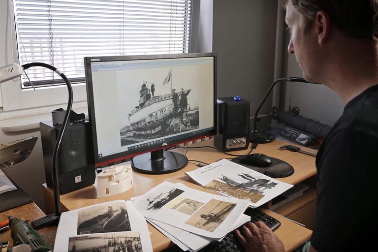 Muž pracuje za stolom s počítačovou obrazovkou zobrazujúcou ponorku.