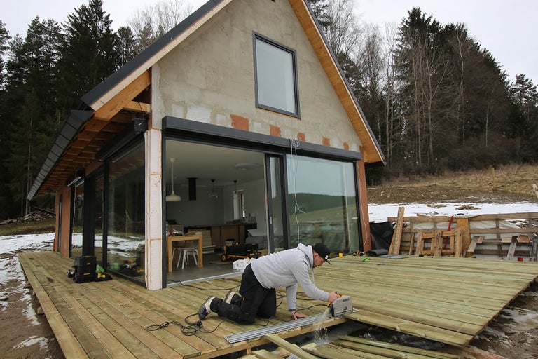 Muž reže drevenú terasu pri dome s posuvnými dverami
