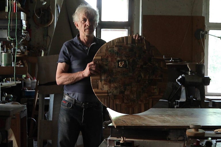 Muž drží okrúhlu drevenú dosku v dielni