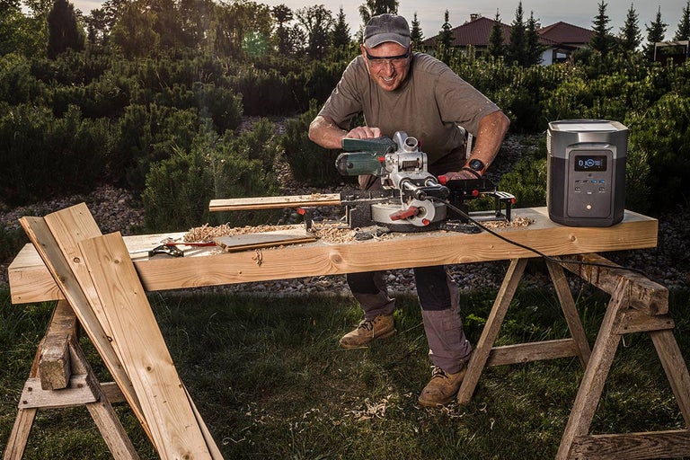Muž pília drevo vonku pomocou pokosovej píly, napájanej elektrárňou