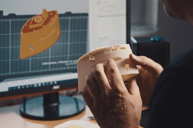 Muž drží 3D tlačený model pred monitorom počítača