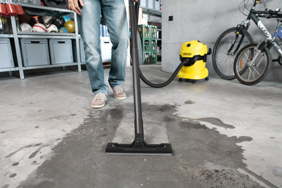 Osoba vysáva mokré nečistoty mokro-suchým vysávačom v garáži.