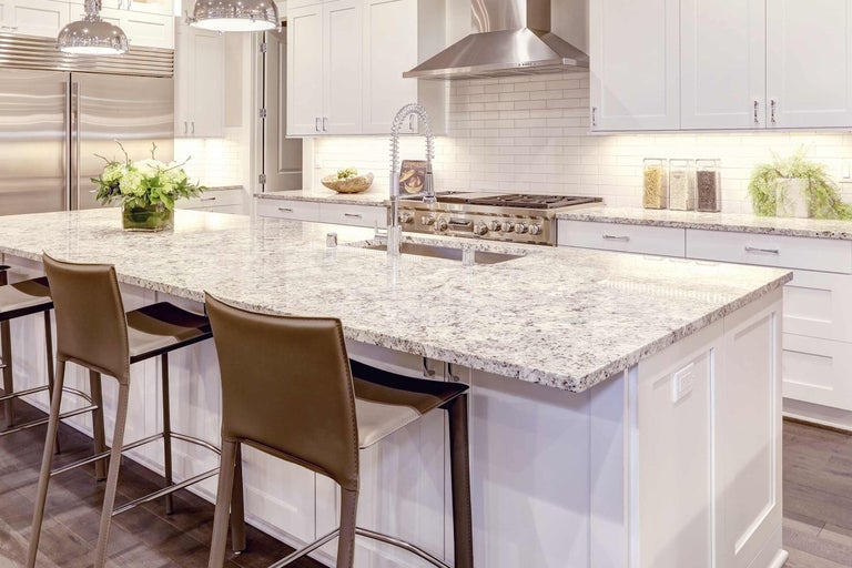 Svetlá kuchyňa s kuchynským ostrovom, žulovou pracovnou doskou, drezom a barovými stoličkami.