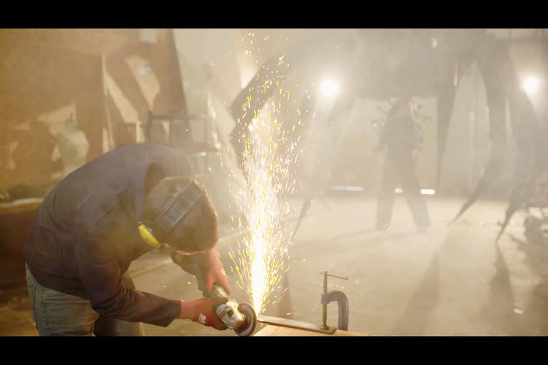 Robotník používa uhlovú brúsku v dielni, odlietajú iskry.