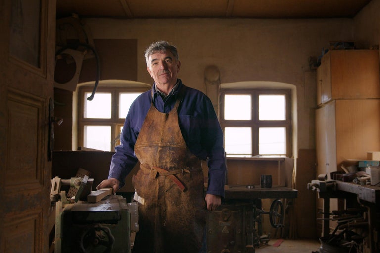 Dielňa so remeselníkom v koženej zástere stojacim pri pracovnom stole