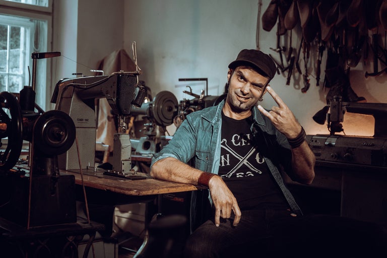 Muž sedí za stolom so šijacími strojmi v dielni.